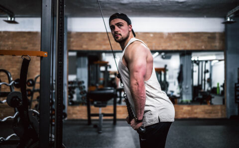 Man exercising with cable machine in gym.