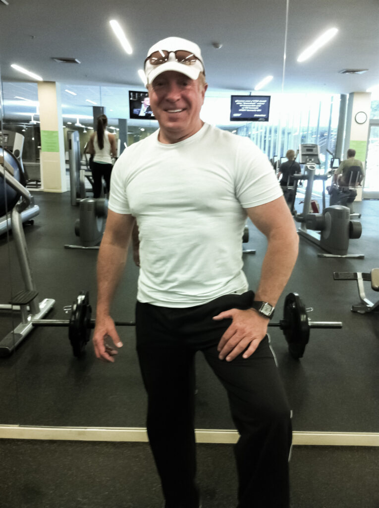 David Hoptar - Scottsdale AZ Personal Trainer A man in white shirt standing next to two barbells.